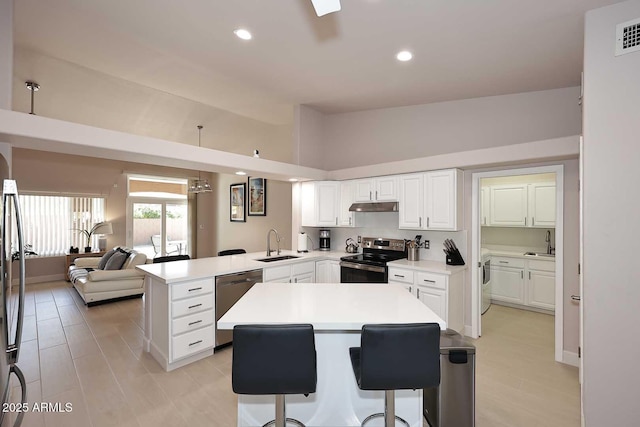 kitchen with a peninsula, lofted ceiling, a sink, stainless steel appliances, and under cabinet range hood