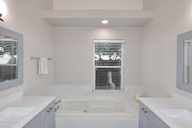 full bath featuring a sink, two vanities, and a tub with jets