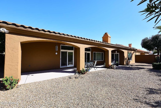 back of property with stucco siding, a patio area, and a chimney