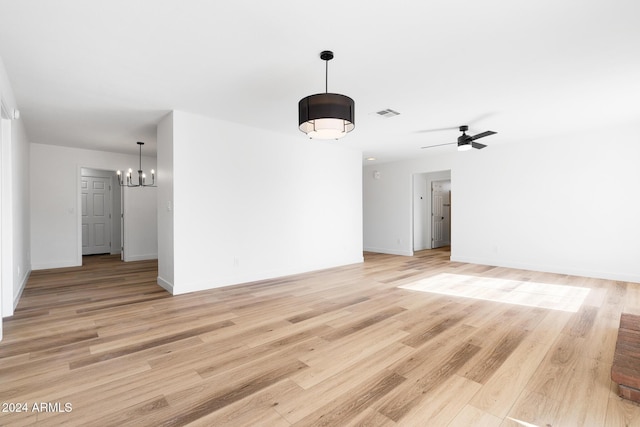 spare room with ceiling fan with notable chandelier and light wood-type flooring