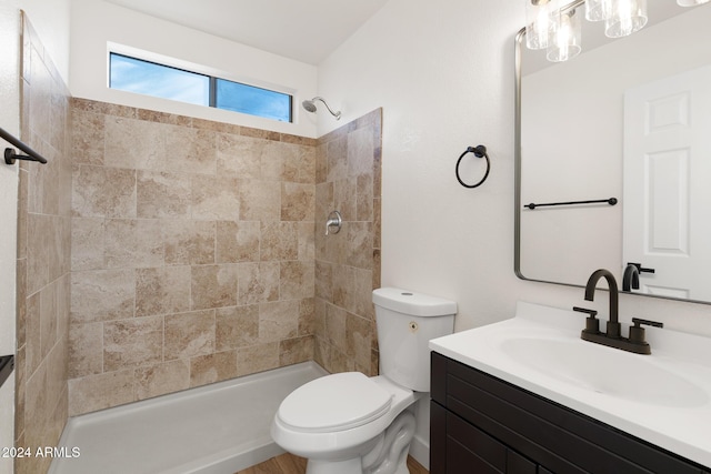 bathroom with a tile shower, toilet, and vanity