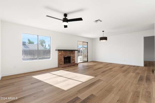 unfurnished living room featuring ceiling fan, light wood-type flooring, and a brick fireplace