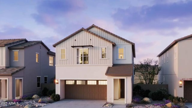 view of front of house with concrete driveway, a tile roof, an attached garage, board and batten siding, and stucco siding