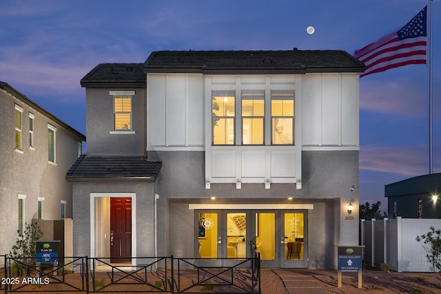 back of house at dusk with board and batten siding, fence, and stucco siding