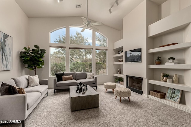 carpeted living room with built in shelves, ceiling fan, a healthy amount of sunlight, and rail lighting