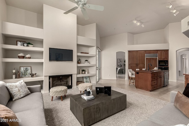 living room featuring ceiling fan, built in features, sink, and a high ceiling