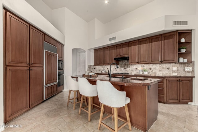 kitchen featuring sink, a towering ceiling, an island with sink, a breakfast bar area, and black appliances