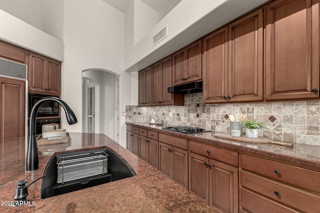 kitchen with sink, decorative backsplash, a towering ceiling, paneled fridge, and stainless steel gas cooktop