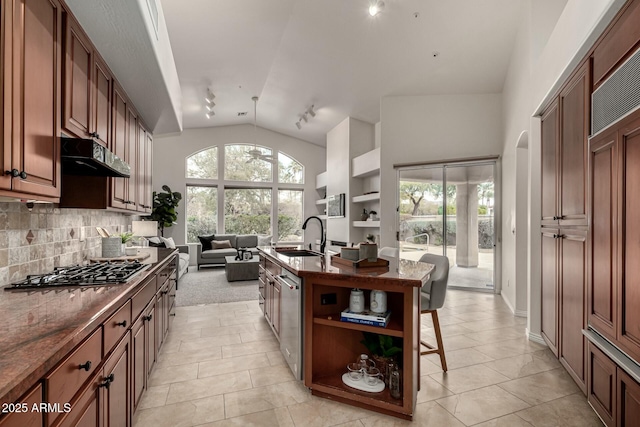 kitchen featuring stainless steel appliances, tasteful backsplash, lofted ceiling, a kitchen island with sink, and a breakfast bar