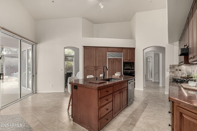 kitchen featuring sink, built in appliances, a towering ceiling, an island with sink, and a breakfast bar area