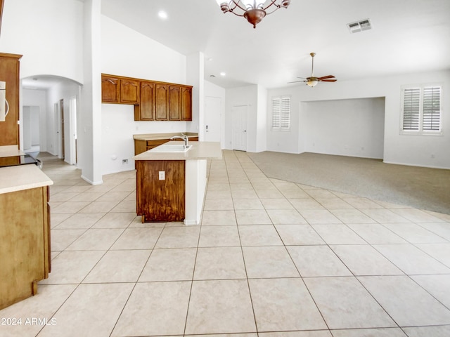 kitchen with a center island with sink, light tile patterned floors, ceiling fan with notable chandelier, and high vaulted ceiling