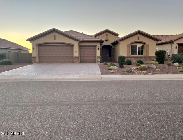 mediterranean / spanish home featuring stucco siding, an attached garage, decorative driveway, stone siding, and a tiled roof
