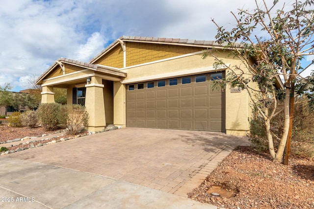 view of front facade featuring an attached garage, a tiled roof, decorative driveway, and stucco siding