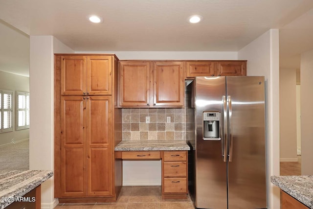 kitchen with light tile patterned floors, stainless steel fridge, light stone counters, tasteful backsplash, and built in desk