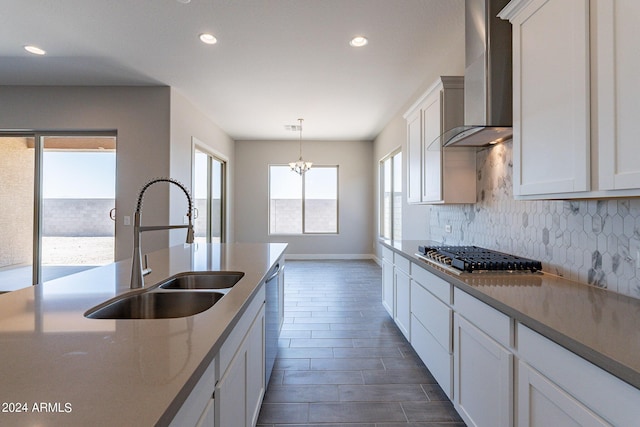 kitchen featuring wall chimney range hood, stainless steel appliances, backsplash, sink, and pendant lighting