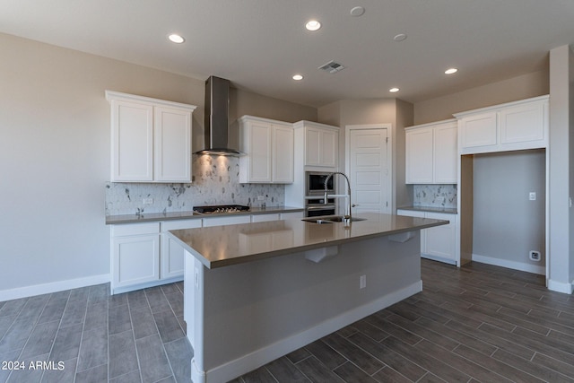 kitchen featuring an island with sink, tasteful backsplash, appliances with stainless steel finishes, and wall chimney exhaust hood