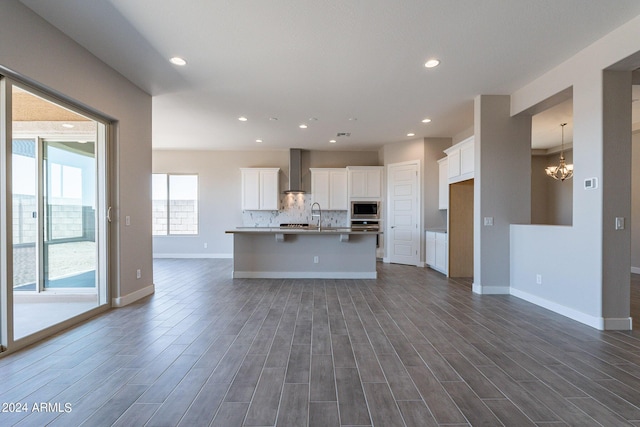 kitchen featuring wall chimney range hood, stainless steel appliances, a kitchen island with sink, hardwood / wood-style floors, and white cabinets