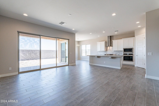 kitchen with wall chimney range hood, hardwood / wood-style flooring, an island with sink, white cabinets, and appliances with stainless steel finishes