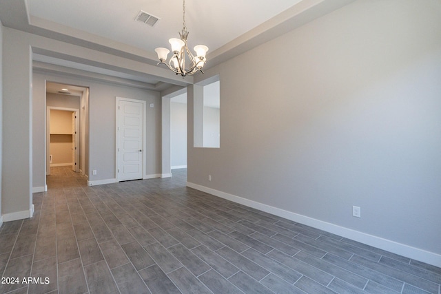 unfurnished room featuring a raised ceiling, dark hardwood / wood-style flooring, and a chandelier