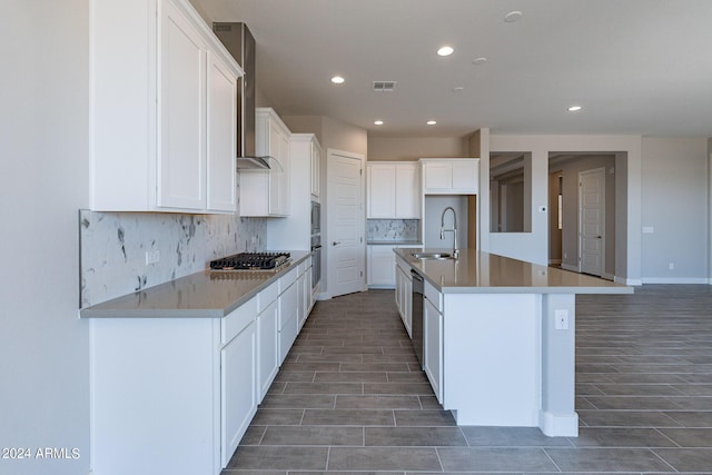 kitchen featuring an island with sink, backsplash, sink, white cabinets, and appliances with stainless steel finishes