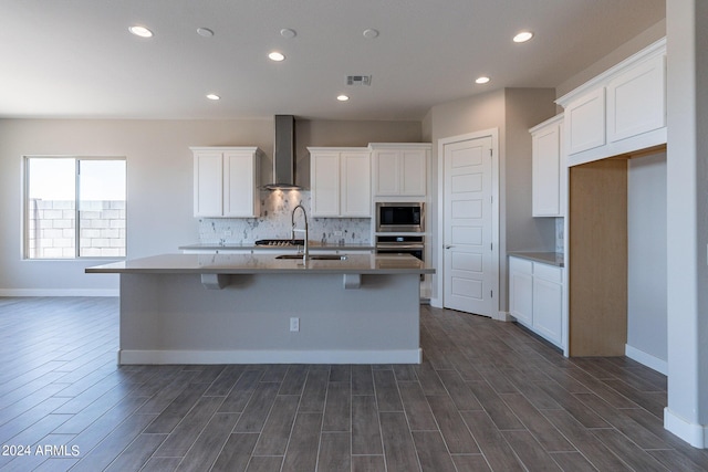 kitchen featuring tasteful backsplash, a center island with sink, wall chimney range hood, sink, and appliances with stainless steel finishes