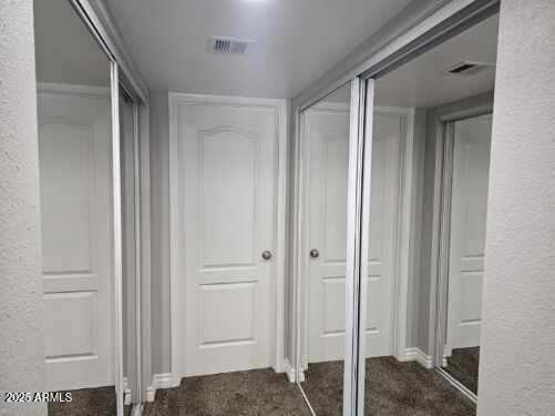 hall with a textured wall, carpet floors, and visible vents