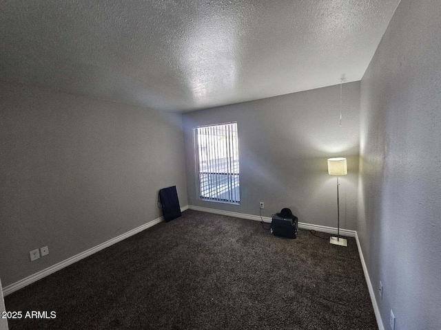 empty room with a textured ceiling, baseboards, and dark carpet