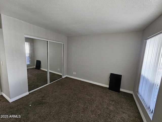 unfurnished bedroom with dark colored carpet, a textured ceiling, a closet, and baseboards