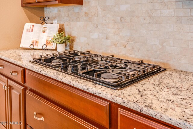 20742 E Mockingbird Dr, Queen Creek, AZ 85142 - kitchen with light stone counters, black gas cooktop, brown cabinetry, and decorative backsplash