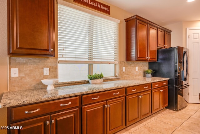 20742 E Mockingbird Dr, Queen Creek, AZ 85142 - kitchen with black refrigerator with ice dispenser, light stone counters, brown cabinetry, decorative backsplash, and light tile patterned floors