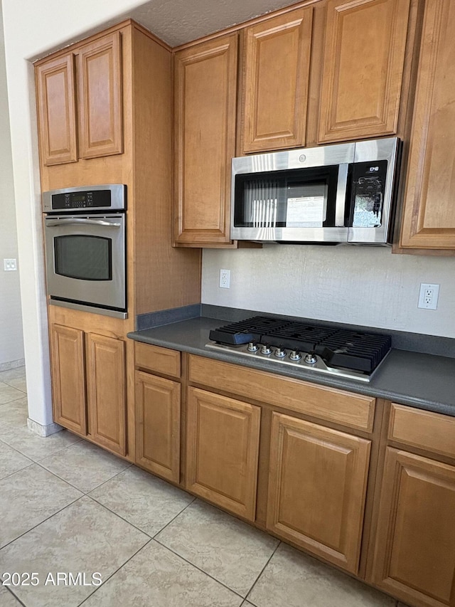 33512 N 24th Ln, Phoenix, AZ 85085 - kitchen with stainless steel appliances, dark countertops, light tile patterned flooring, and brown cabinetry