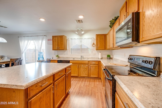 kitchen featuring black electric range, sink, a kitchen island, light hardwood / wood-style floors, and decorative backsplash