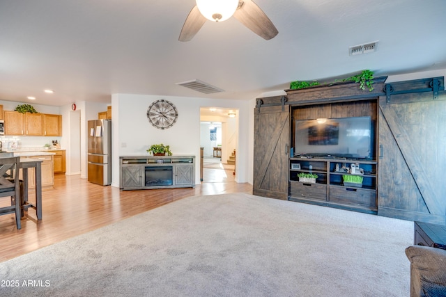 living room with ceiling fan, a barn door, and light wood-type flooring