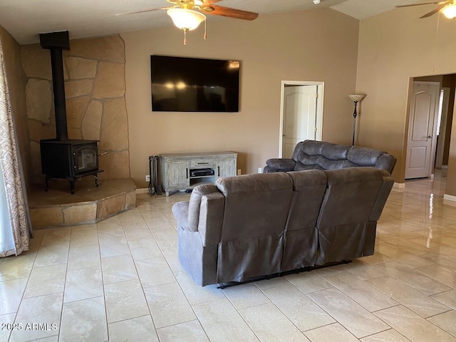 living room with a wood stove, ceiling fan, baseboards, light tile patterned flooring, and high vaulted ceiling