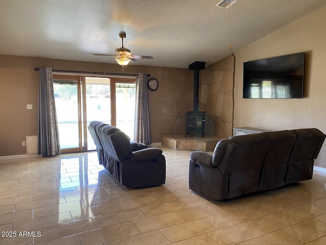 living area featuring visible vents, ceiling fan, baseboards, a wood stove, and light tile patterned flooring