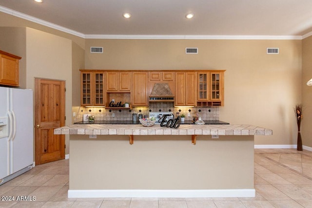 kitchen featuring a kitchen bar, white refrigerator with ice dispenser, stainless steel stove, custom range hood, and ornamental molding