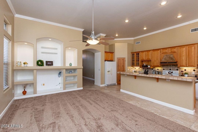 kitchen with decorative backsplash, tile countertops, custom range hood, light colored carpet, and white appliances