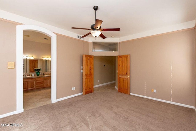 unfurnished bedroom featuring light carpet, ensuite bath, and ceiling fan