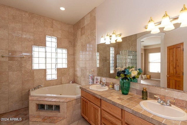 bathroom featuring vanity, a relaxing tiled tub, and tile walls