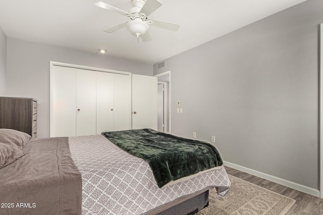 bedroom with wood finished floors, a ceiling fan, visible vents, baseboards, and a closet