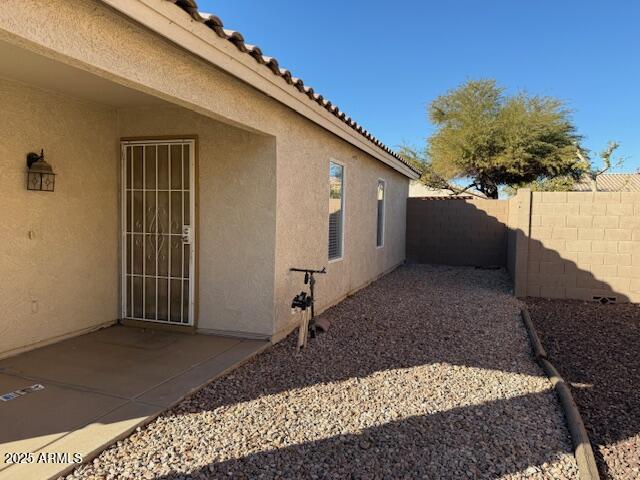 view of side of property with a tiled roof, stucco siding, a fenced backyard, and a patio area