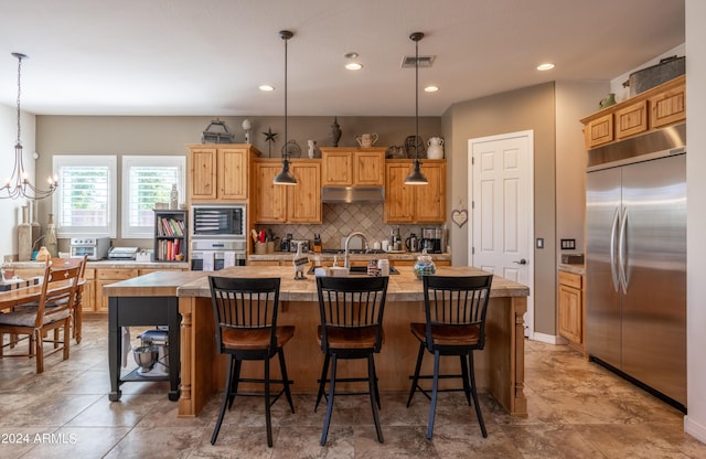 kitchen featuring sink, built in appliances, an island with sink, pendant lighting, and decorative backsplash