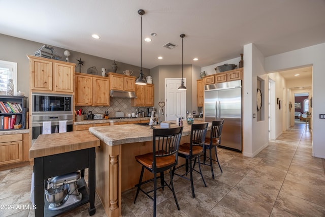 kitchen featuring pendant lighting, light brown cabinetry, decorative backsplash, a kitchen island with sink, and black appliances