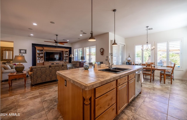 kitchen featuring sink, ceiling fan with notable chandelier, dishwasher, a kitchen island with sink, and decorative light fixtures