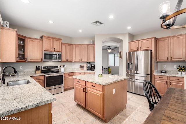 kitchen with light tile patterned flooring, a kitchen island, appliances with stainless steel finishes, sink, and light stone countertops