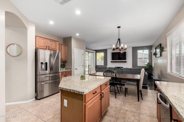 kitchen with light tile patterned floors, stainless steel appliances, a center island, a notable chandelier, and light stone countertops