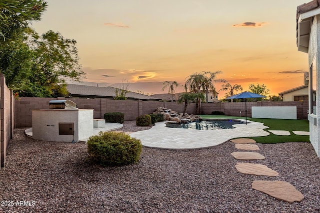 yard at dusk featuring an outdoor kitchen, a fenced in pool, and a patio