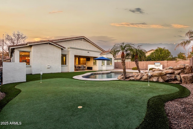 back house at dusk with a fenced in pool and a patio