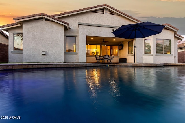 pool at dusk with ceiling fan and a patio area