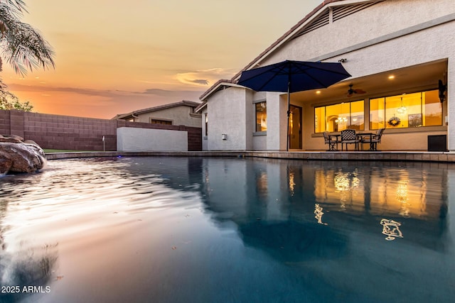 pool at dusk featuring a patio, pool water feature, and ceiling fan